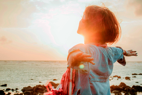 persona con los brazos extendidos frente al mar en el atardecer